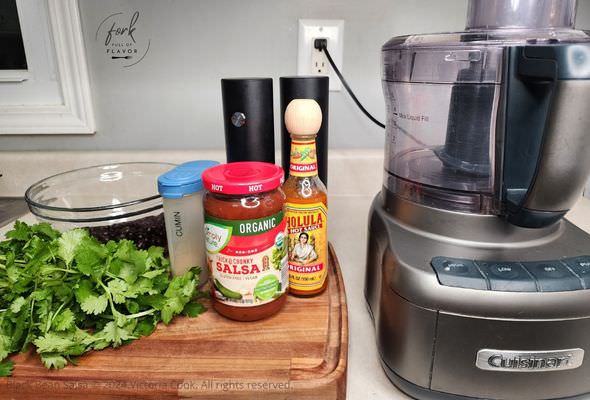 Ingredients needed for making Black Bean Salsa: black beans, cilantro, cumin, salsa, Cholula, olive oil, salt & pepper and a food processor to blend it all together.