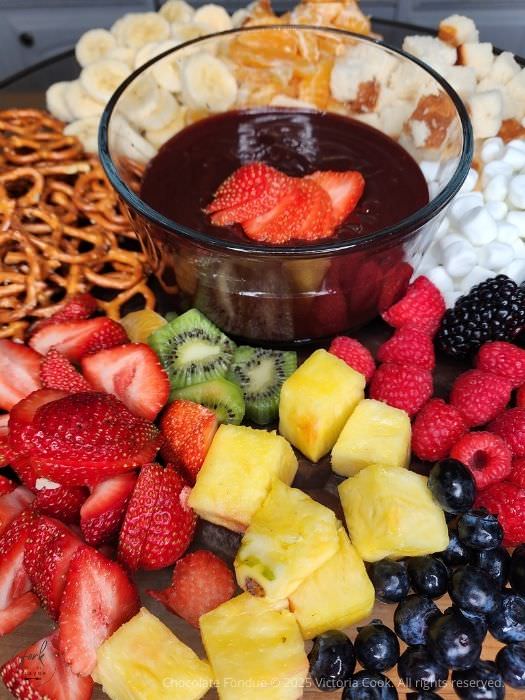 A platter of fresh berries, pineapple, pretzels and marshmallows surrounding some decadent chocolate fondue.