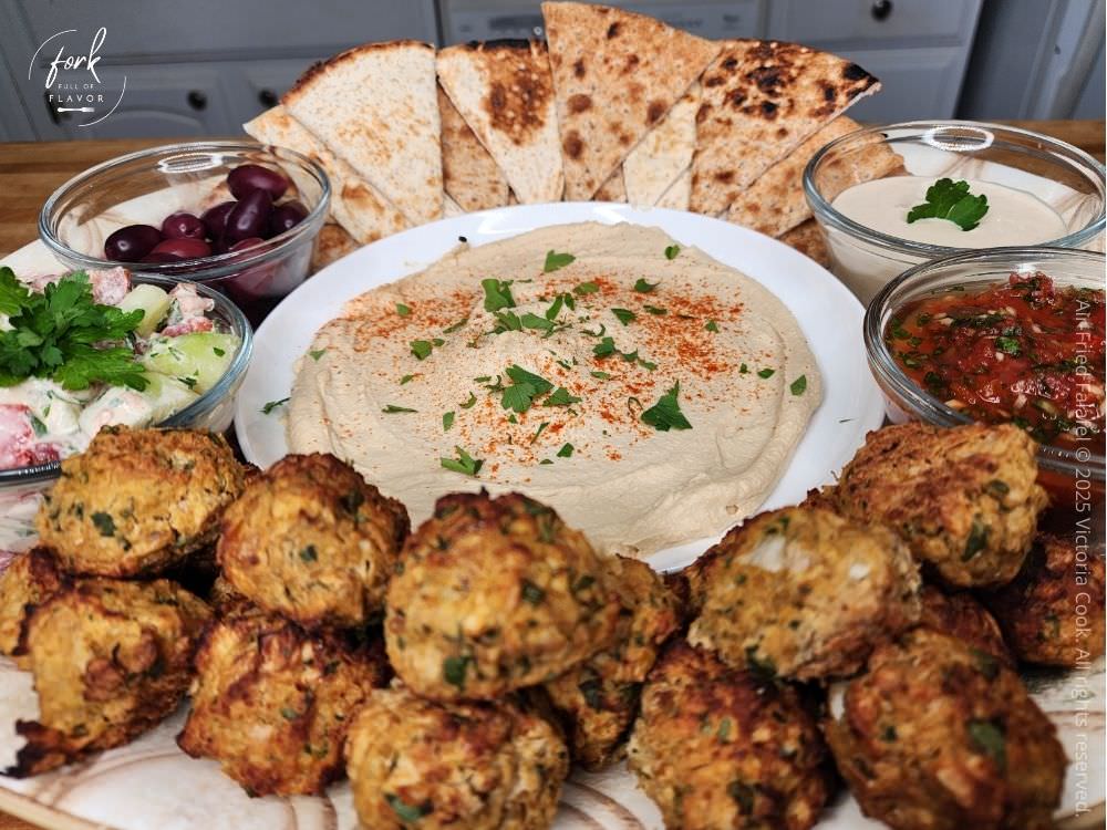 A platter of falafel, pita bread, hummus, tahini sauce, middle eastern hot sauce, and calamata olives creating a delicious