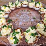 A round tray of Mexican Street Corn Deviled Eggs garnished with corn and cilantro and rimmed with Tajin.