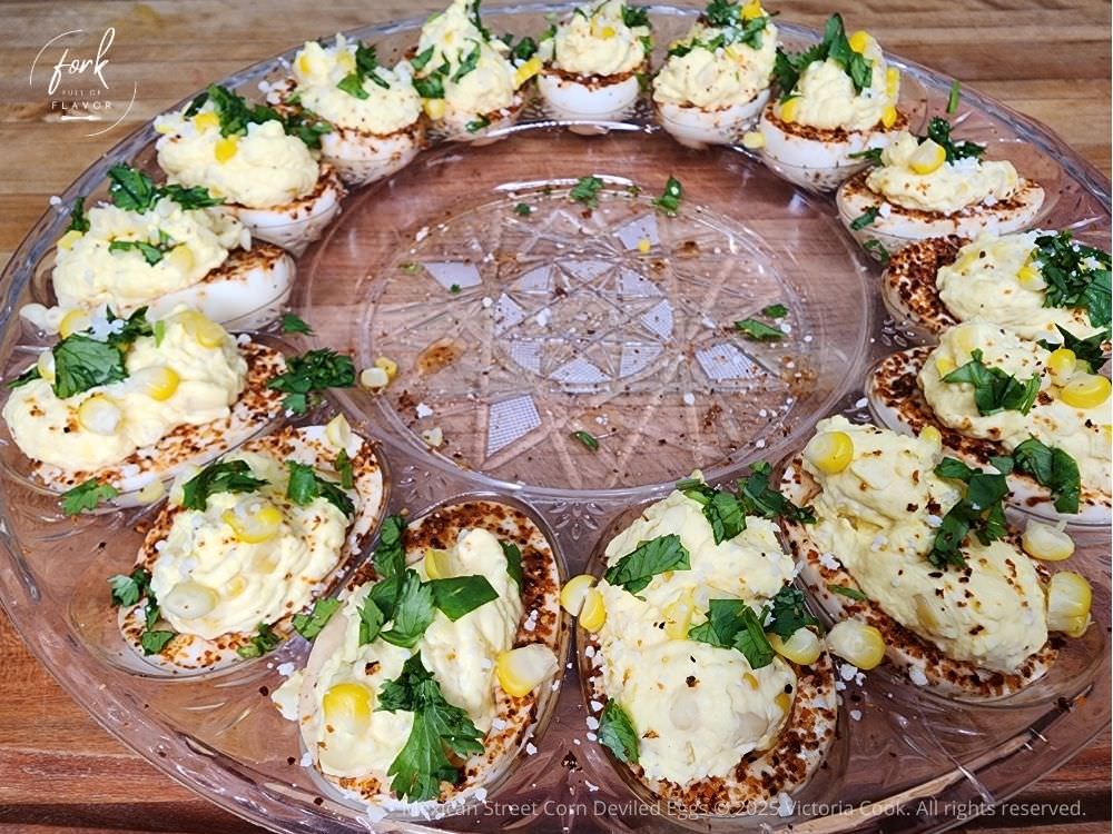 A round tray of Mexican Street Corn Deviled Eggs garnished with corn and cilantro and rimmed with Tajin.