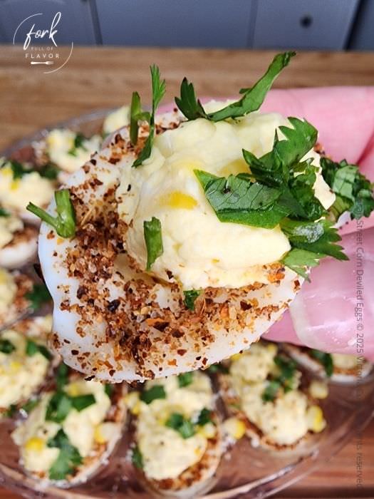 A single Mexican Street Corn deviled egg in front of a plate of them.