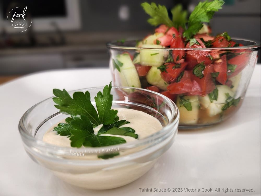 Tahini sauce in a bowl with a small salad of tomatoes, cucumbers, and parsley tossed in the tahini sauce